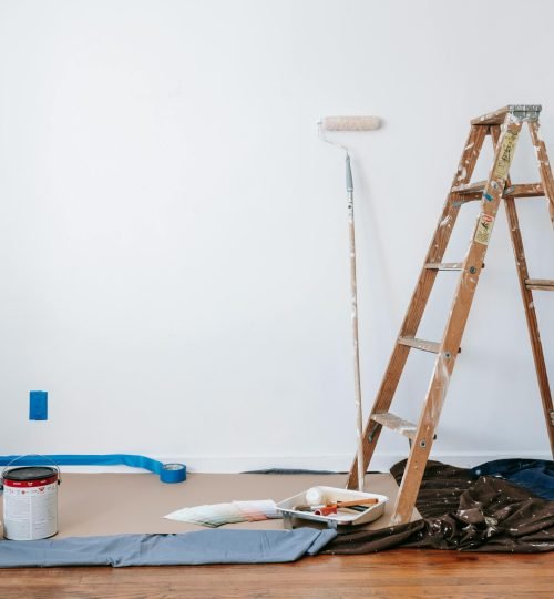 A room prepared for renovation with a ladder, paint supplies, and drop cloth.